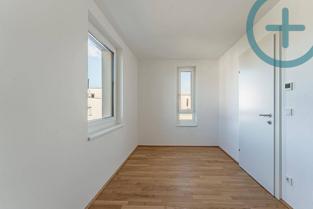 Helles Schlafzimmer mit Parkettboden und zwei Fenstern, bereit zur individuellen Gestaltung und Nutzung.