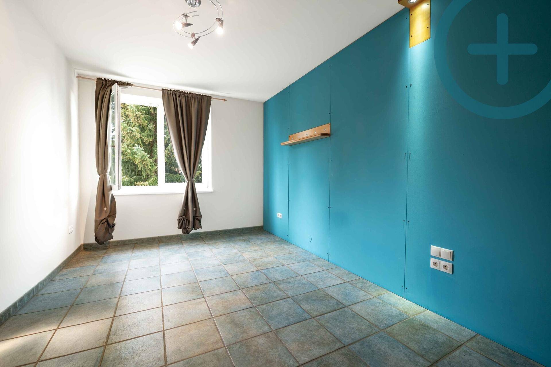 Leeres Zimmer mit blauer Akzentwand, Fenster und grauen Fliesen, bereit zur individuellen Gestaltung.