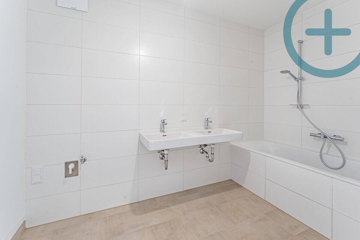 Geräumiges Badezimmer mit Doppelwaschbecken, Badewanne und hellen Fliesen an Wänden und Boden.