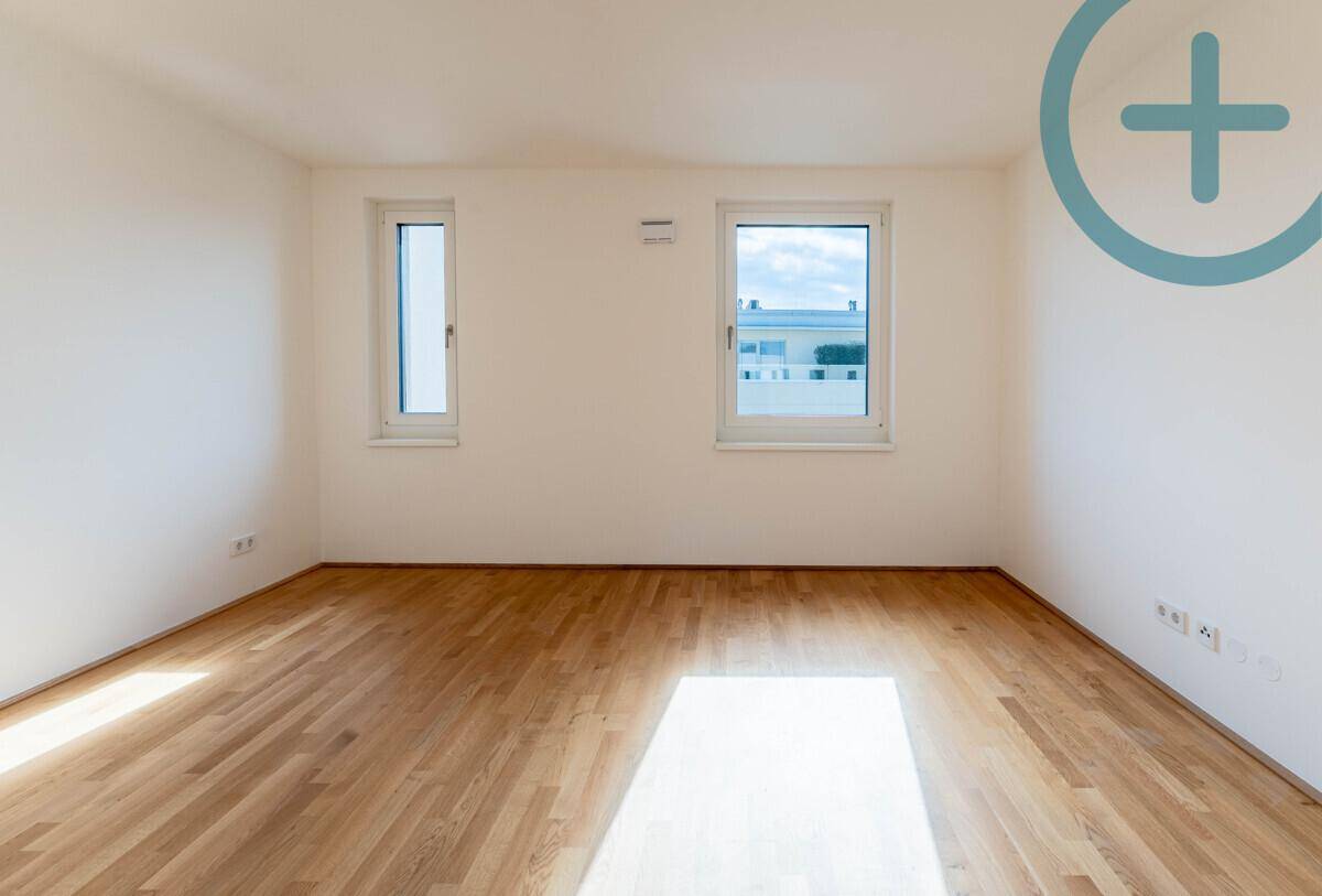Helles Schlafzimmer mit Parkettboden und zwei Fenstern, die für eine angenehme Atmosphäre sorgen.