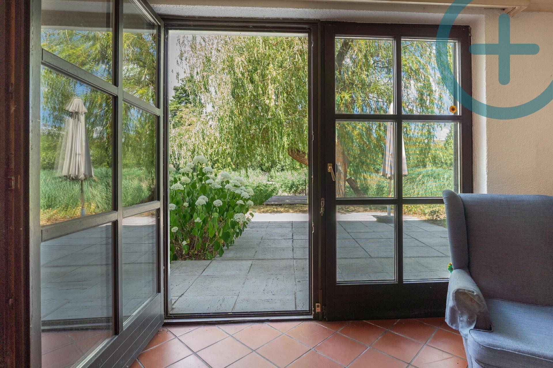 Blick aus dem Innenraum durch große Glastüren auf die Terrasse und den grünen Gartenbereich.