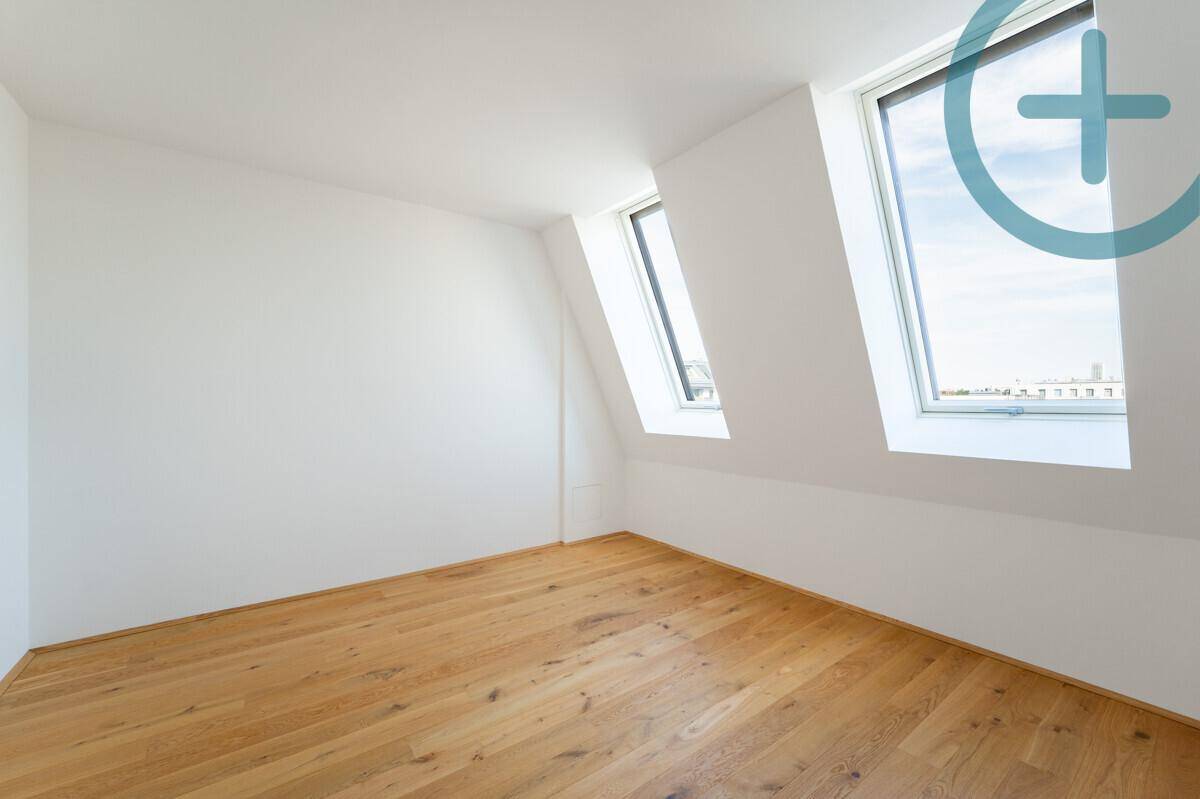 Helles Schlafzimmer im Dachgeschoss mit Holzboden und zwei Dachfenstern.