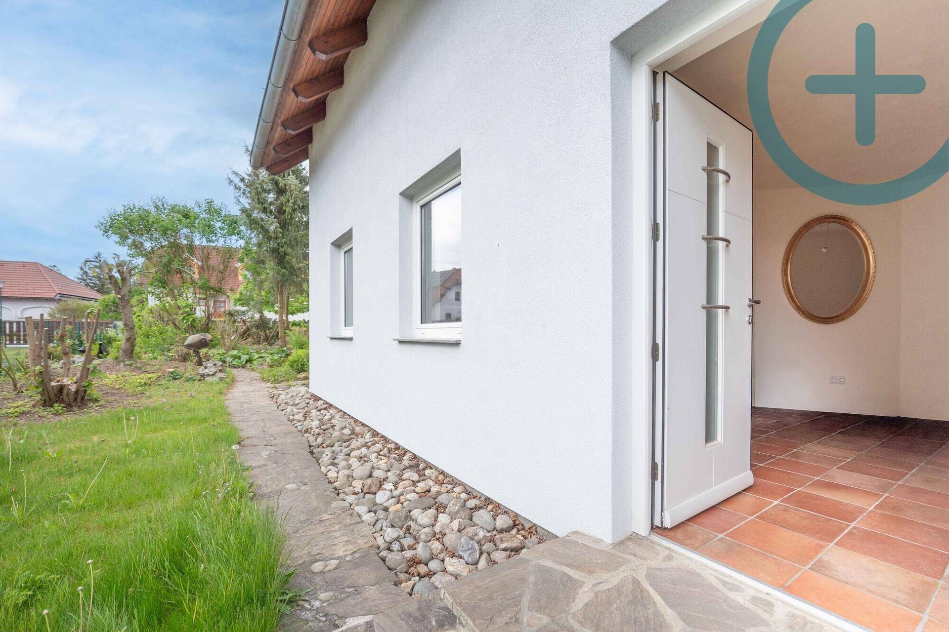 Moderner Hauseingang mit weißer Fassade, stilvoller Tür und gepflegtem Vorgartenbereich.