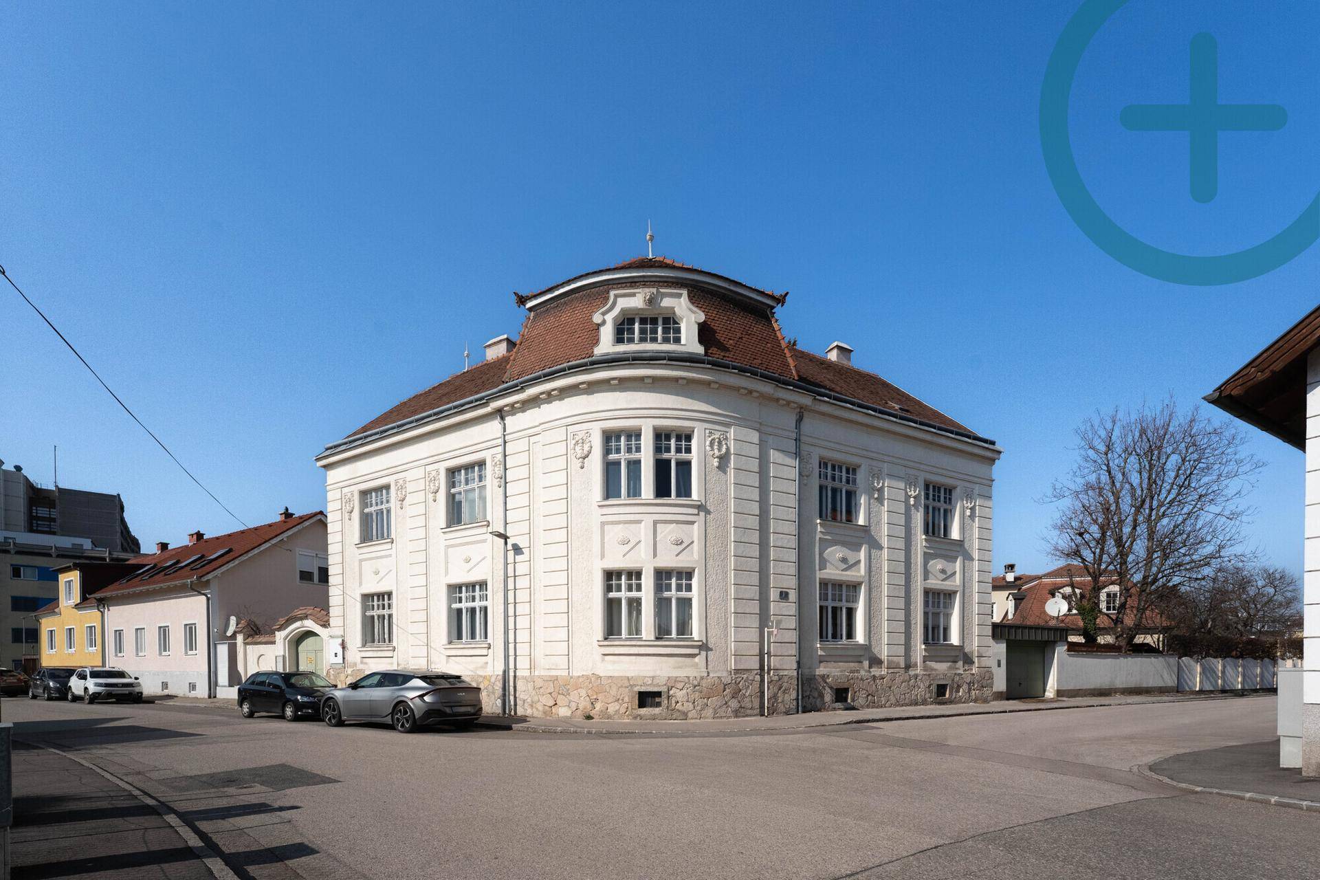 Historisches Eckgebäude mit eleganter weißer Fassade und traditionellem Dach unter blauem Himmel.