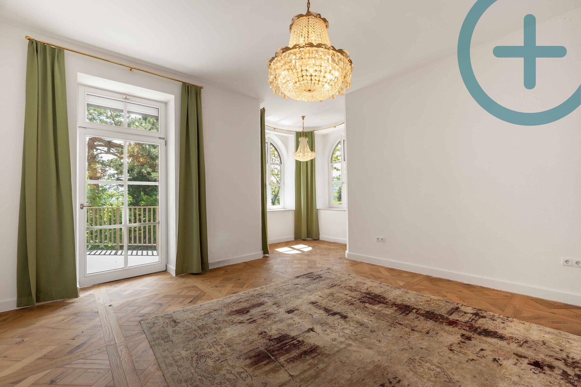Heller Wohnraum mit Fischgrätparkett, Kronleuchter und Zugang zu einem französischen Balkon.
