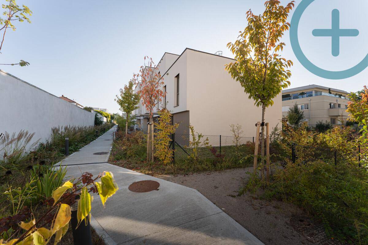 Außenansicht eines modernen Wohnkomplexes mit Gehwegen, Bäumen und Grünflächen.