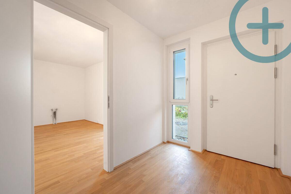 Heller Eingangsbereich mit Parkettboden, Fenster und Zugang zu einem weiteren Zimmer.