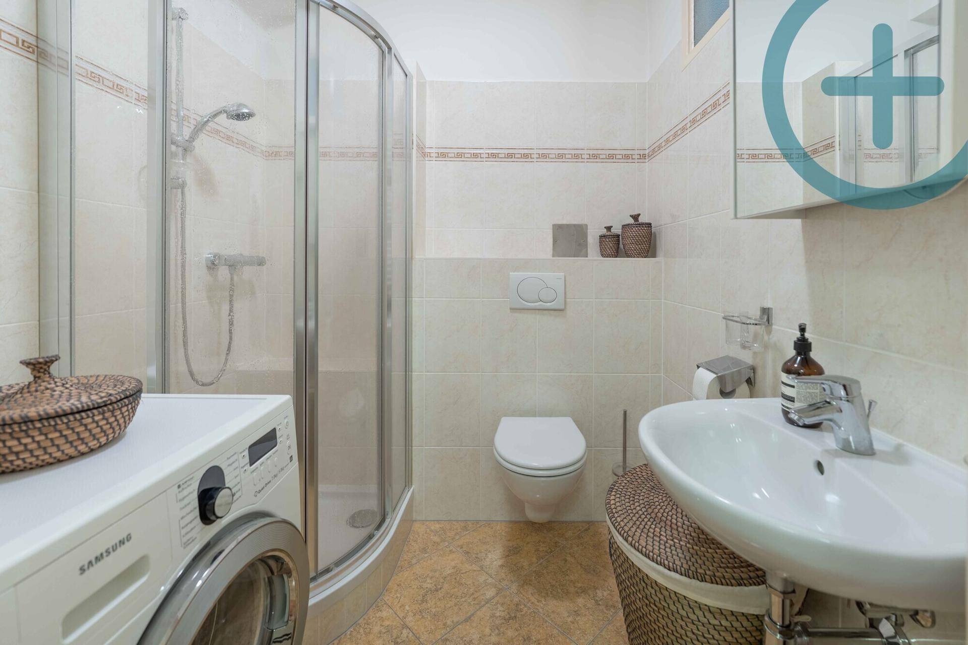 Gefliestes Badezimmer mit Duschkabine, WC, Waschbecken und Waschmaschine.