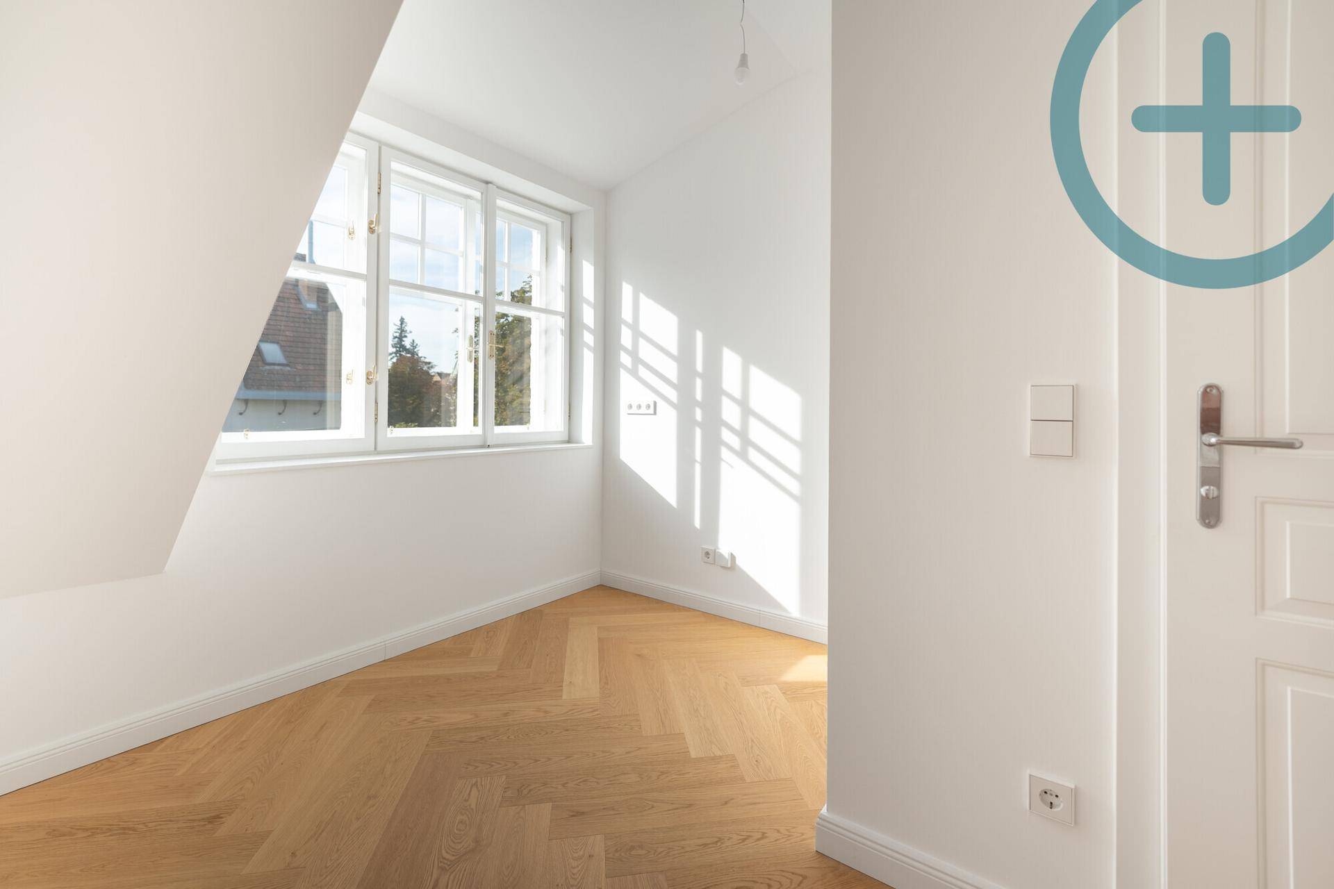 Helles Zimmer mit Fischgrätparkett, Dachschräge und klassischem Fenster.