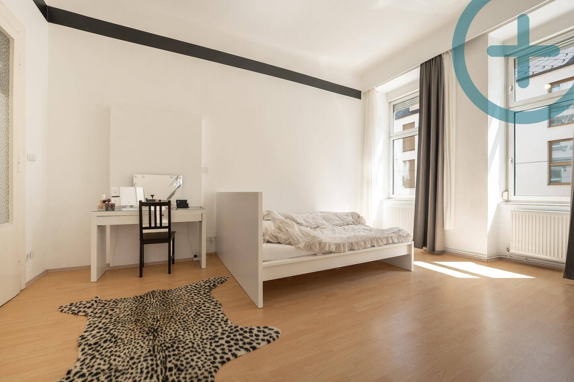 Schlafzimmer mit hellem Laminatboden, Schreibtisch und Fenster mit viel Tageslicht.