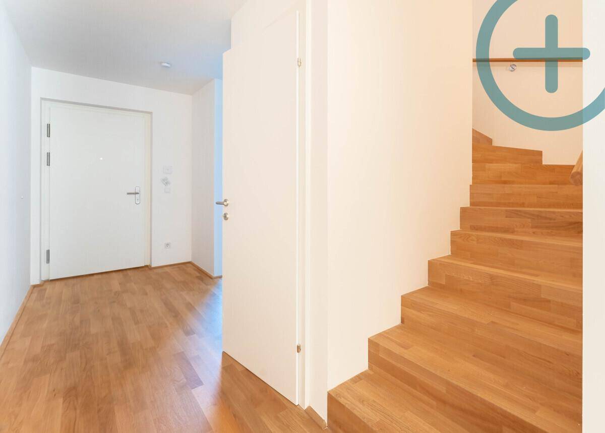 Heller Eingangsbereich mit Holztreppe und Parkettboden, der zu den oberen Etagen führt.