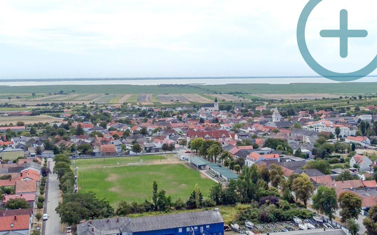 Panoramablick auf eine ländliche Siedlung mit einem See am Horizont und grünen Feldern.