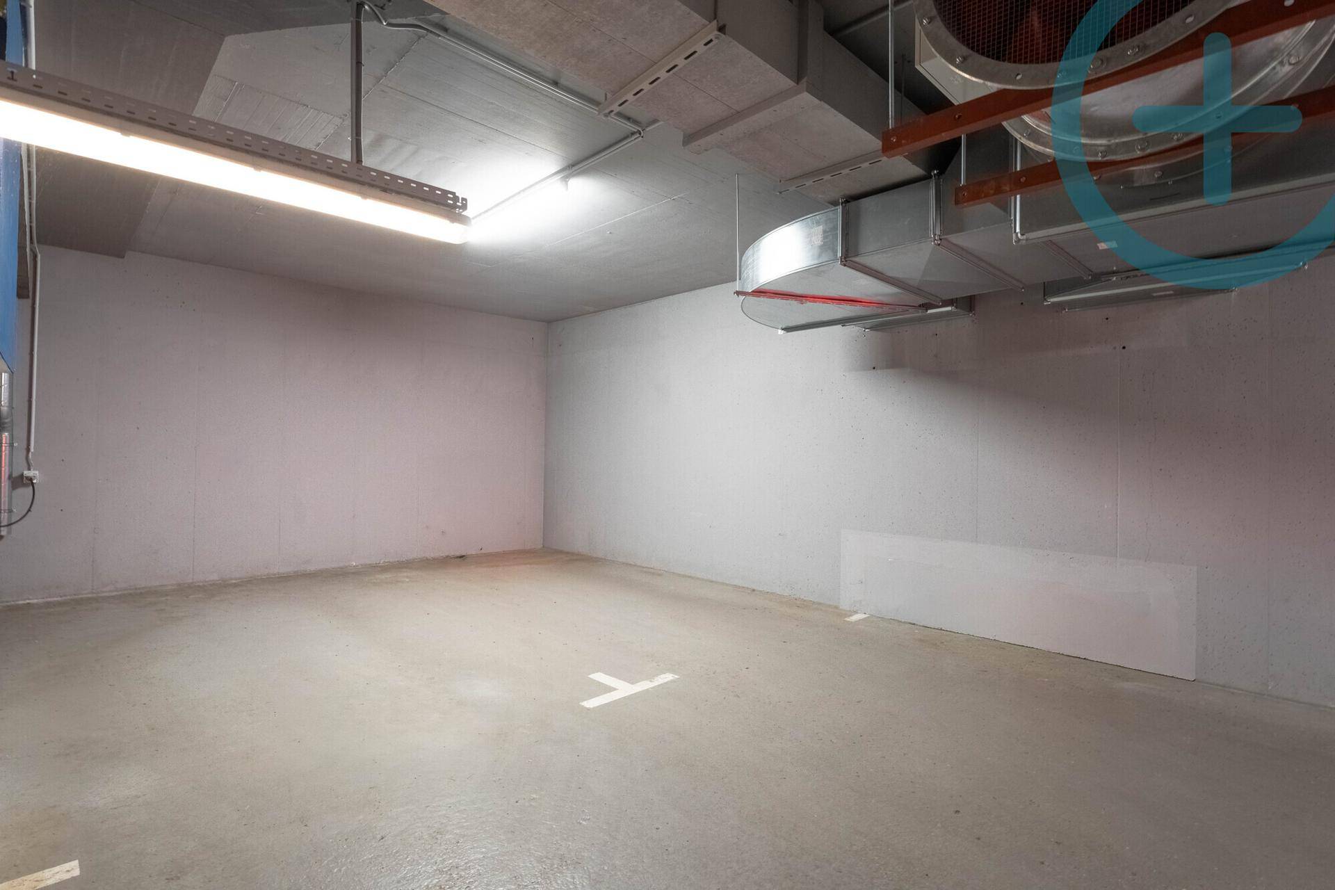 Geräumige Tiefgarage mit Betonboden und sichtbaren Lüftungsrohren an der Decke.