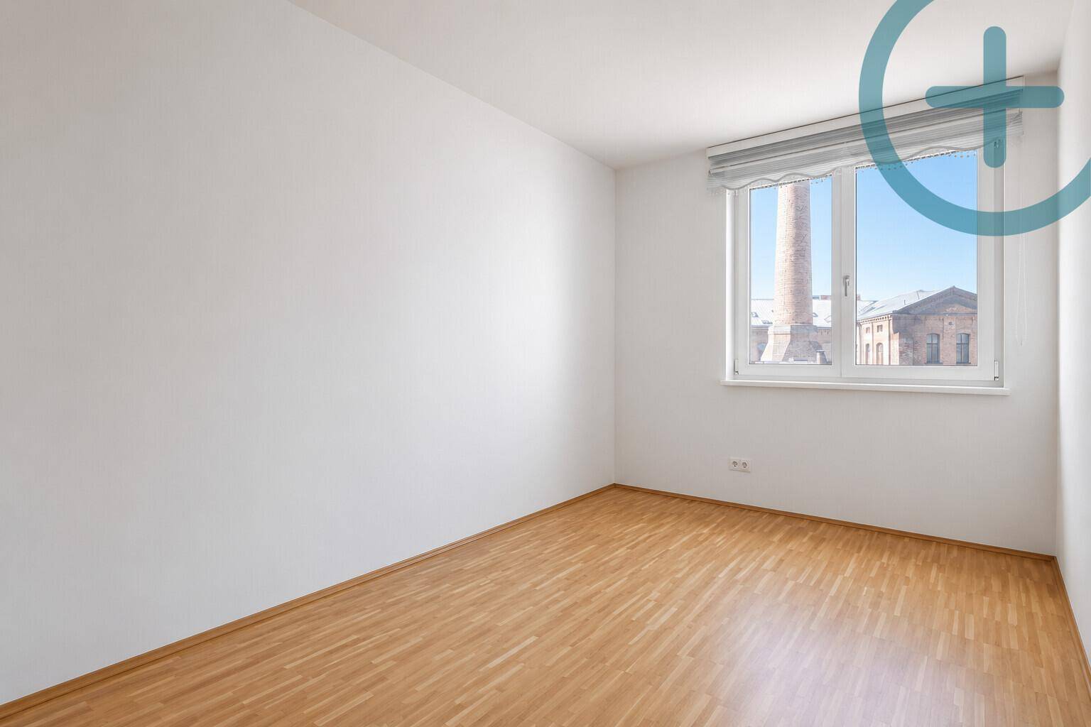Helles Zimmer mit Holzboden und Fenster, das einen Blick auf die Umgebung bietet.