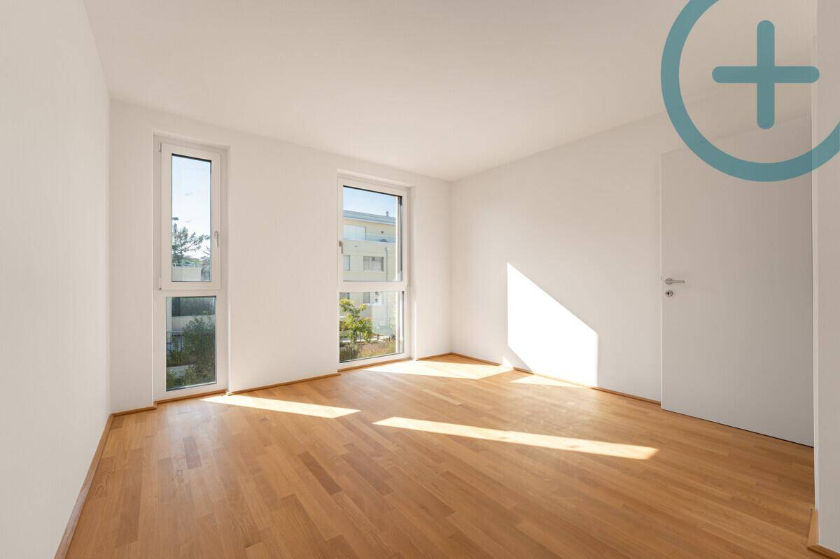 Helles Schlafzimmer mit Parkettboden und zwei Fenstern, die viel Tageslicht hereinlassen.