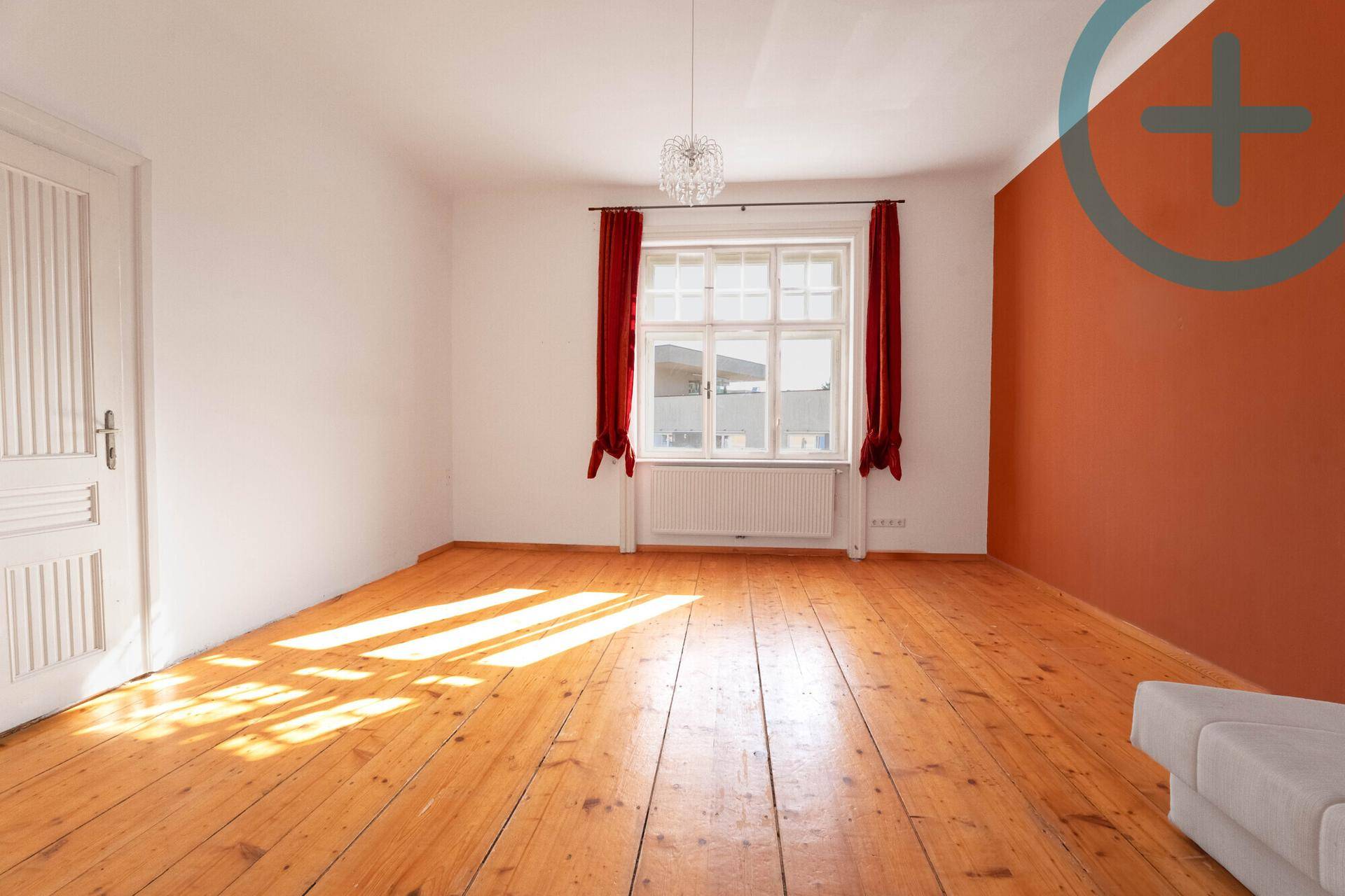 Geräumiger, heller Raum mit Holzdielenboden und einer farbigen Akzentwand.