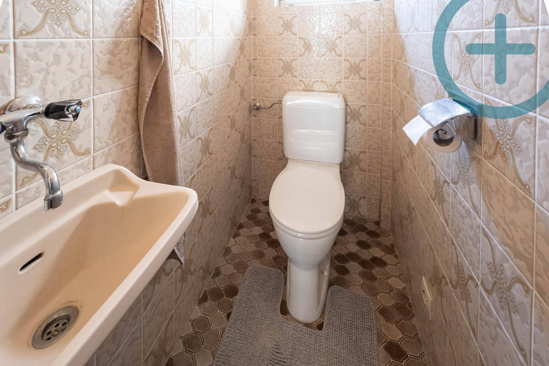 Kleines WC mit Waschbecken und Fliesenboden in neutralen Farbtönen.