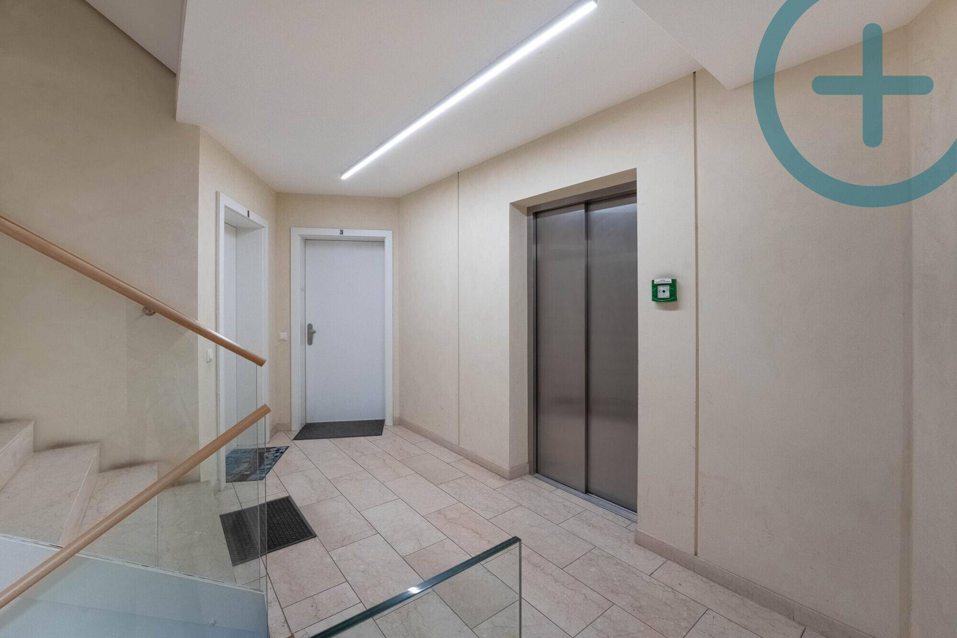 Heller Treppenhausbereich mit Aufzug, Fliesenboden und modernem Glasgeländer.