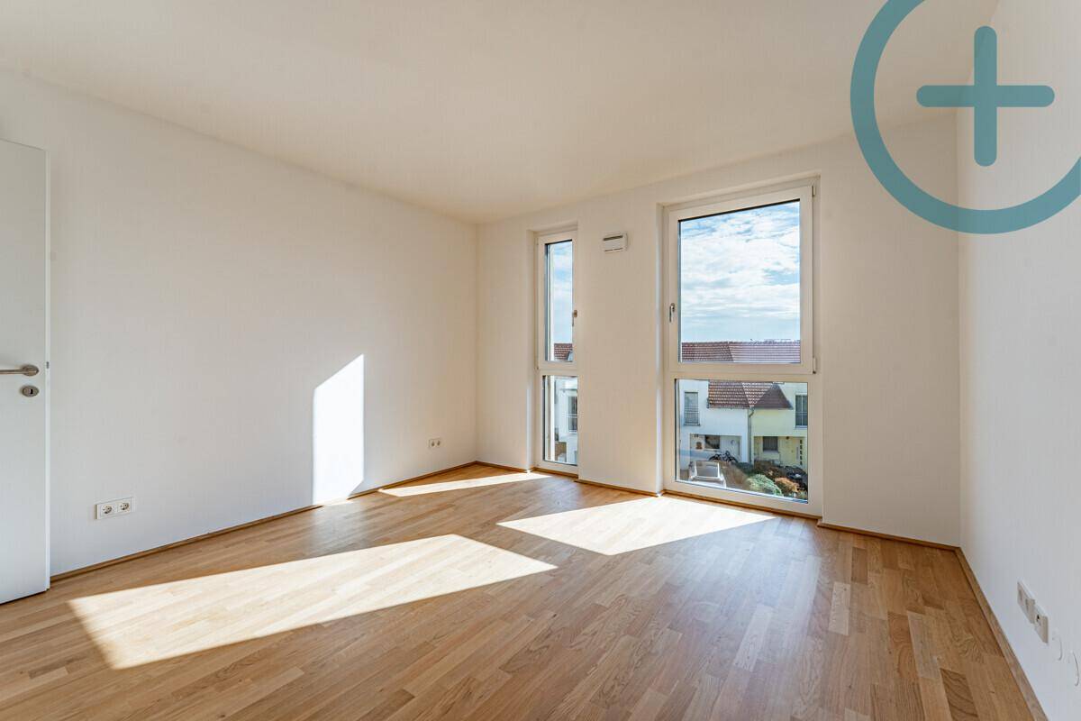 Sonniger Raum mit Parkettboden und großen Fenstern, die einen weiten Blick bieten.