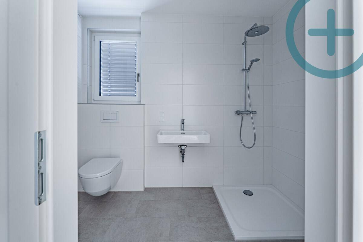 Modernes Badezimmer mit ebenerdiger Dusche, wandhängendem WC und Fenster mit Jalousien.