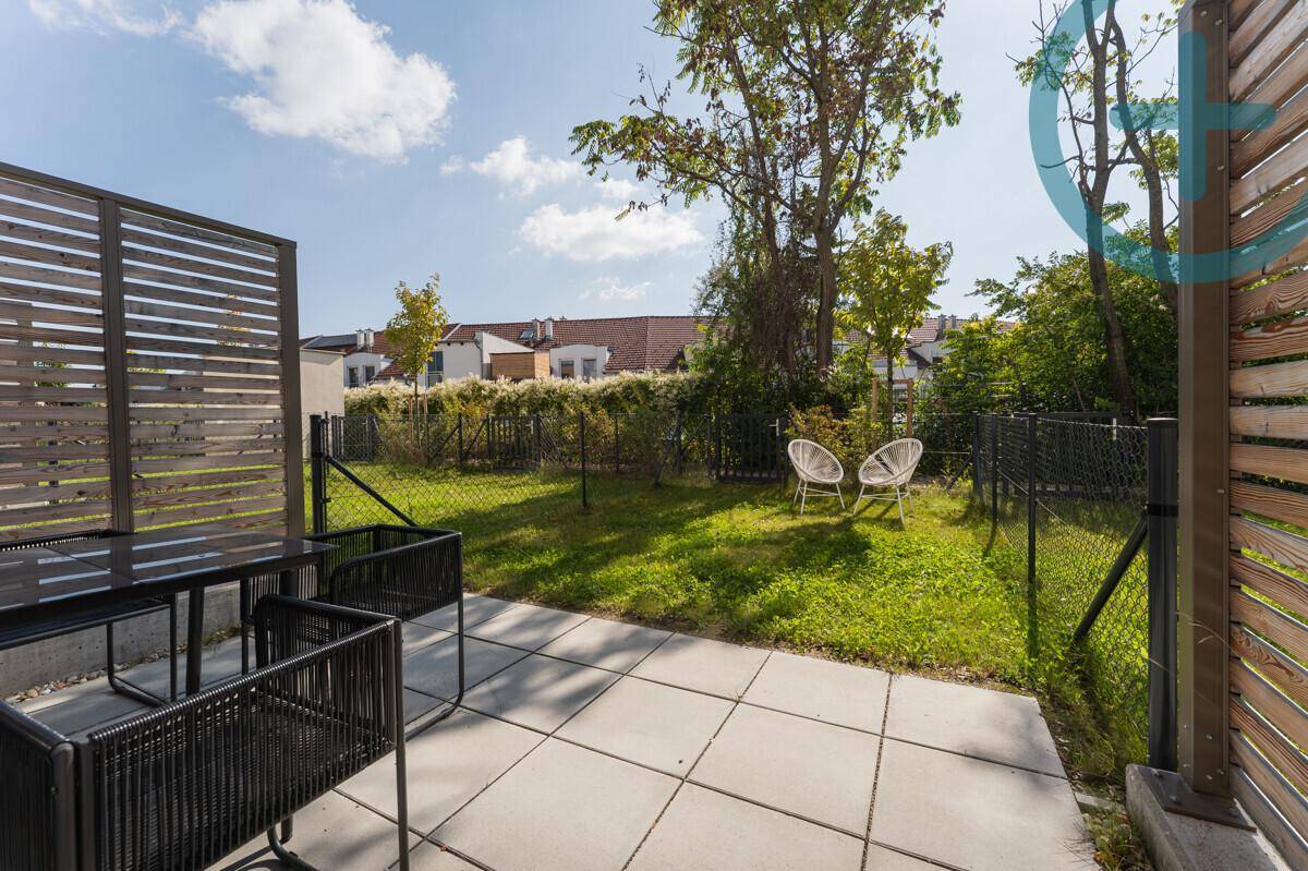 Sonniger Terrassenbereich mit Gartenmöbeln und kleinem Rasen, umgeben von einem Zaun.