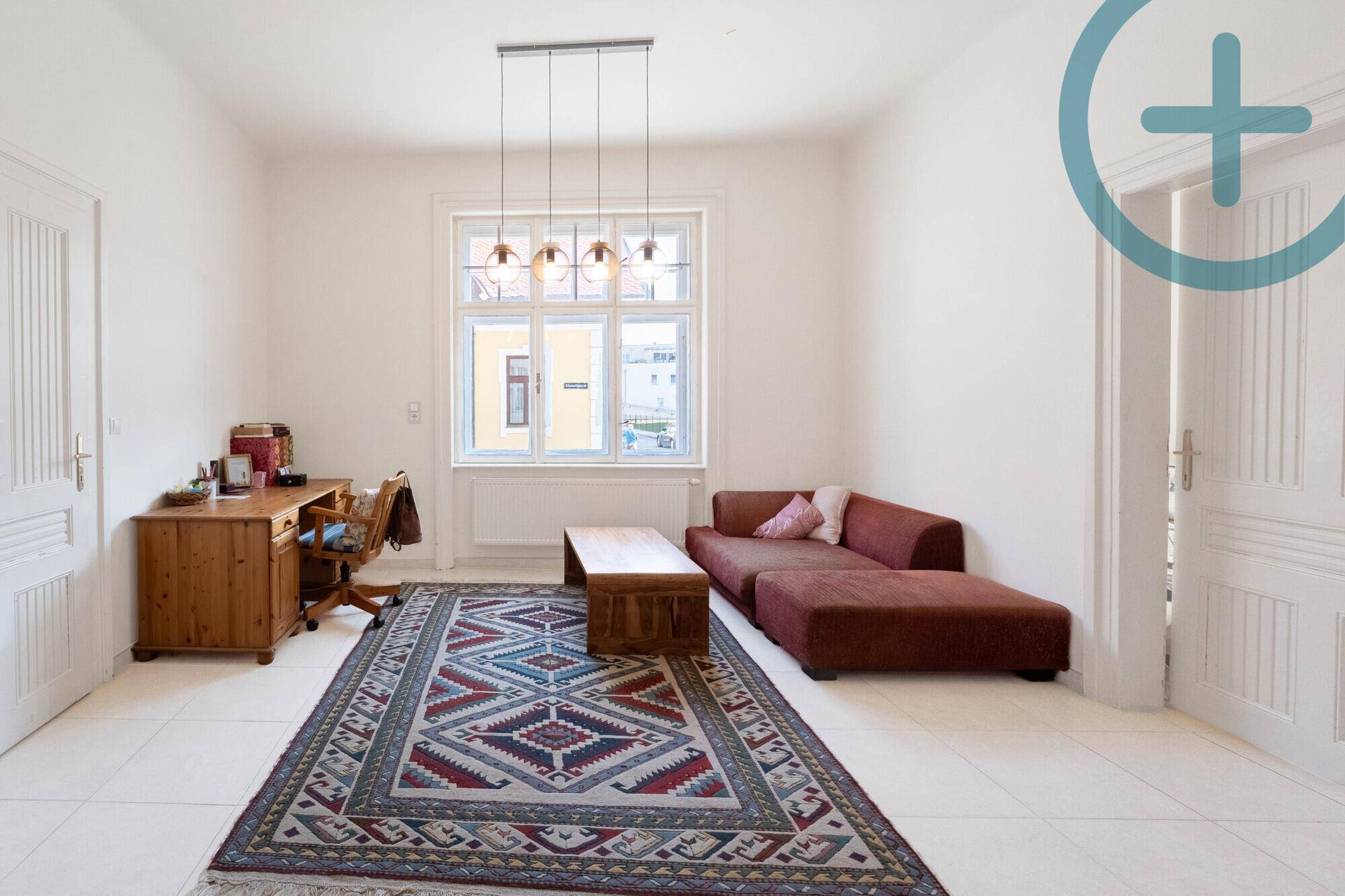 Helles Wohnzimmer mit Schreibtisch, Sofa und einem großen Fenster mit Blick nach draußen.