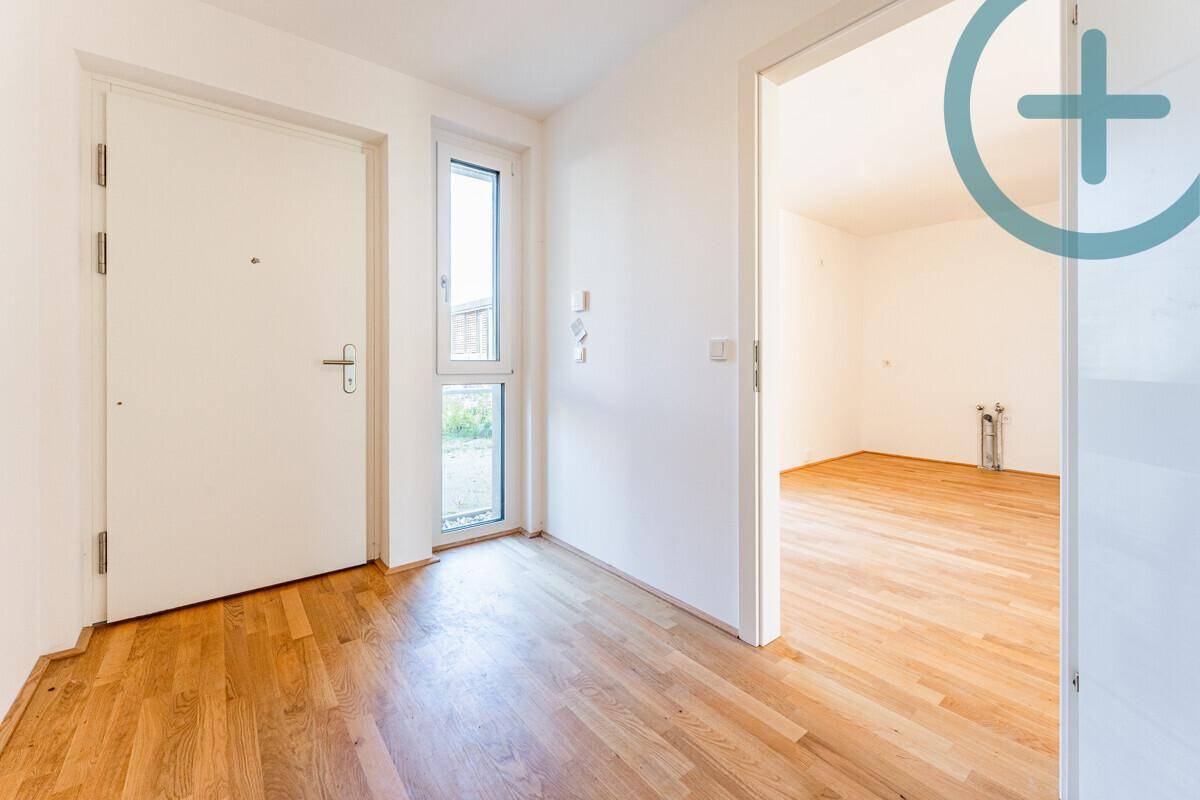 Eingangsbereich mit weißer Haustür, schmalem Fenster und Zugang zu einem weiteren Zimmer.