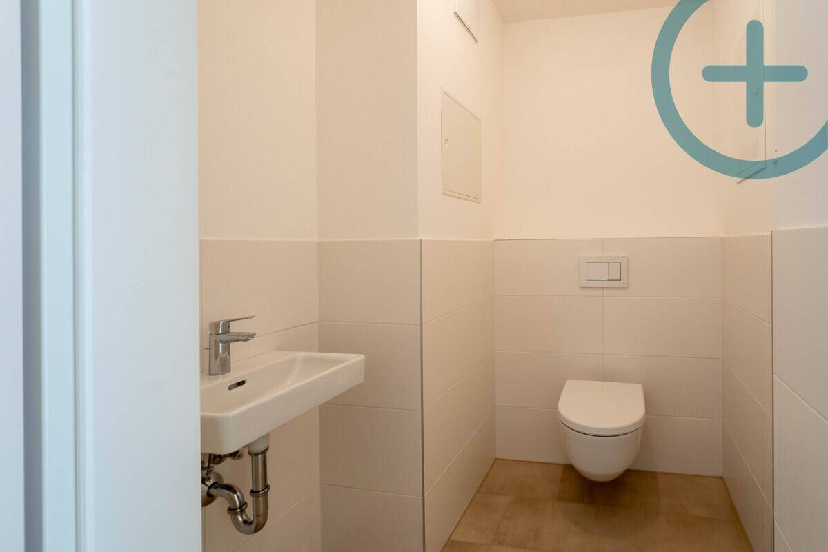 Gäste-WC mit wandhängendem WC, kleinem Waschbecken und hellen Fliesen an den Wänden.