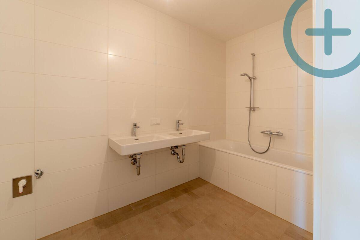 Modernes Badezimmer mit Doppelwaschbecken, Badewanne und hellen, großformatigen Fliesen.