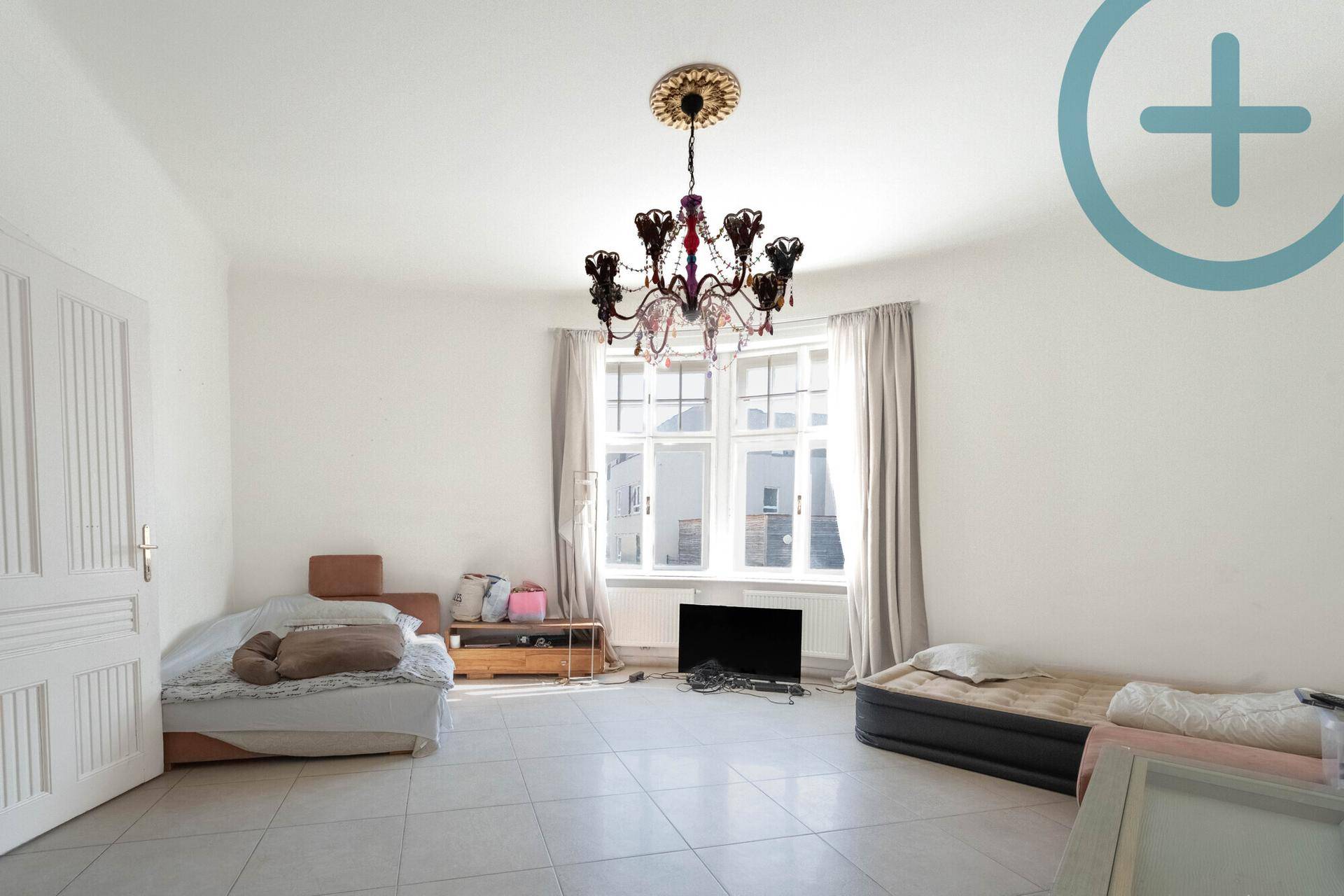 Geräumiges Schlafzimmer mit Fliesenboden, großem Fenster und einem Kronleuchter an der Decke.