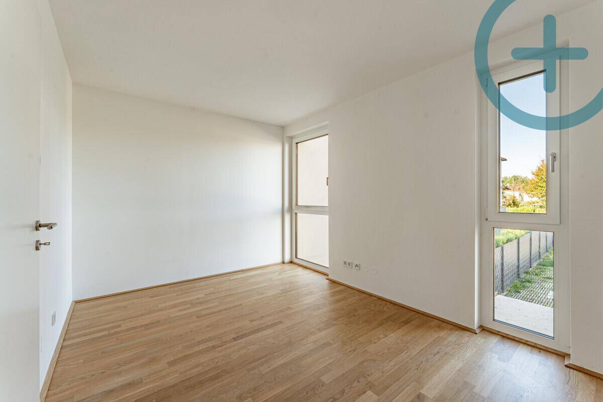 Leeres Schlafzimmer mit Parkettboden und hohen Fenstern, die viel natürliches Licht hereinlassen.