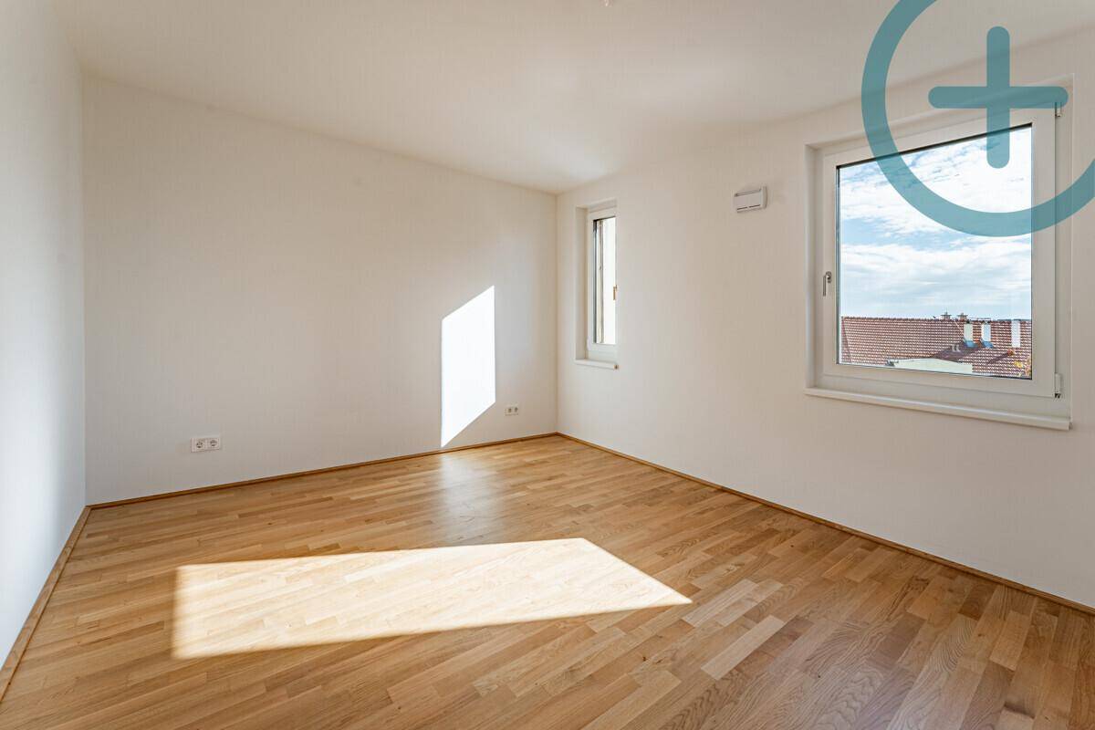 Lichtdurchflutetes Zimmer mit Parkettboden und zwei Fenstern, die einen weiten Blick ermöglichen.