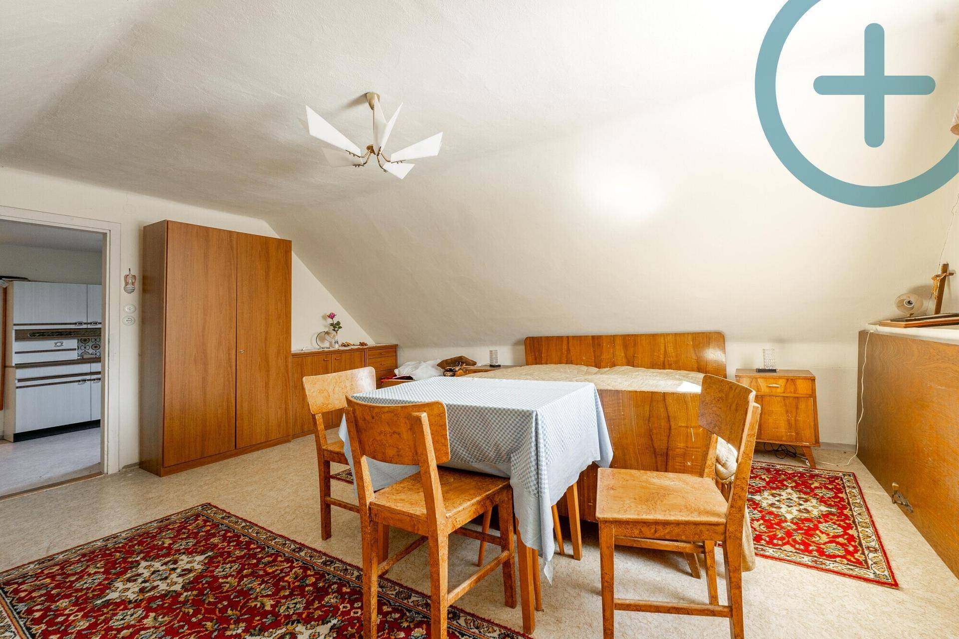 Dachgeschoss-Schlafzimmer mit Doppelbett, Esstisch und Zugang zu einem weiteren Raum.