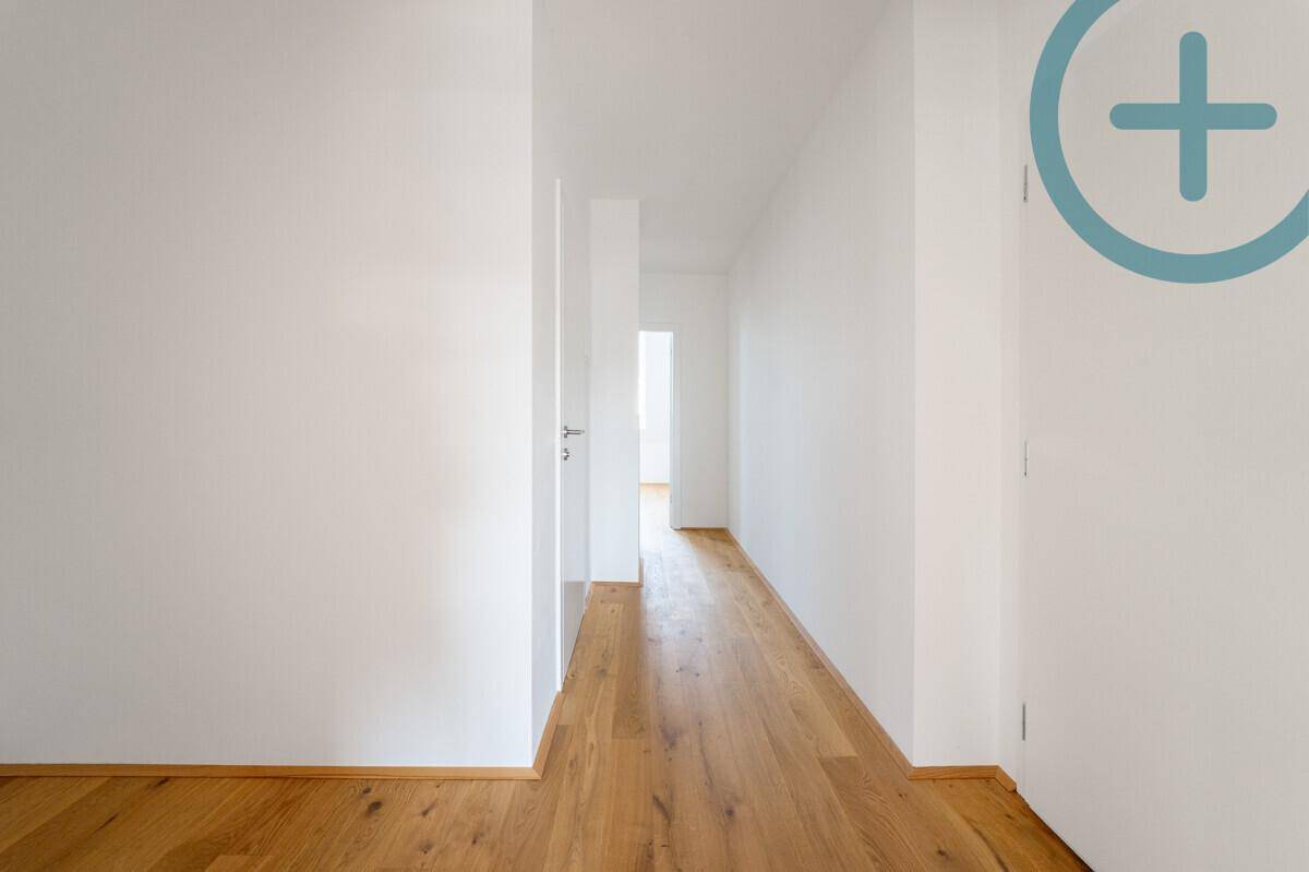 Langer, heller Flur mit Holzboden und weißen Wänden, der zu weiteren Räumen führt.