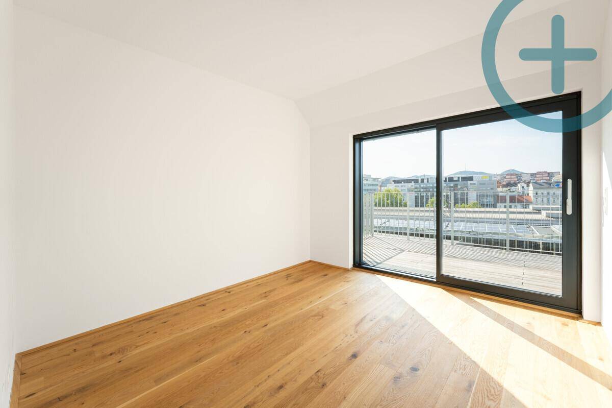 Helles Zimmer mit Holzboden und großer Schiebetür, die Zugang zu einem Balkon bietet.