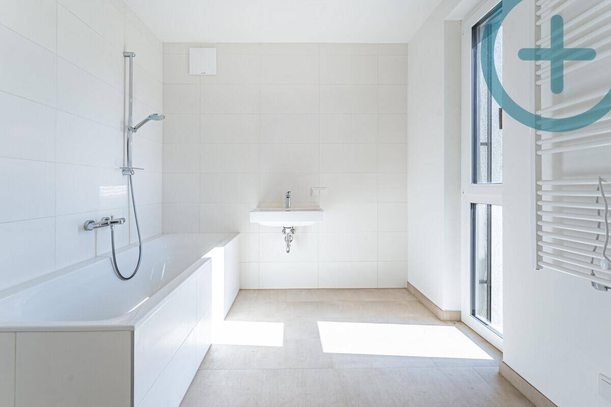 Modernes Badezimmer mit Badewanne, Waschbecken, Fenster und beheiztem Handtuchhalter.