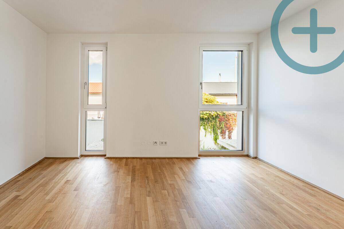 Helles Schlafzimmer mit Parkettboden und zwei Fenstern, eines davon als französischer Balkon.