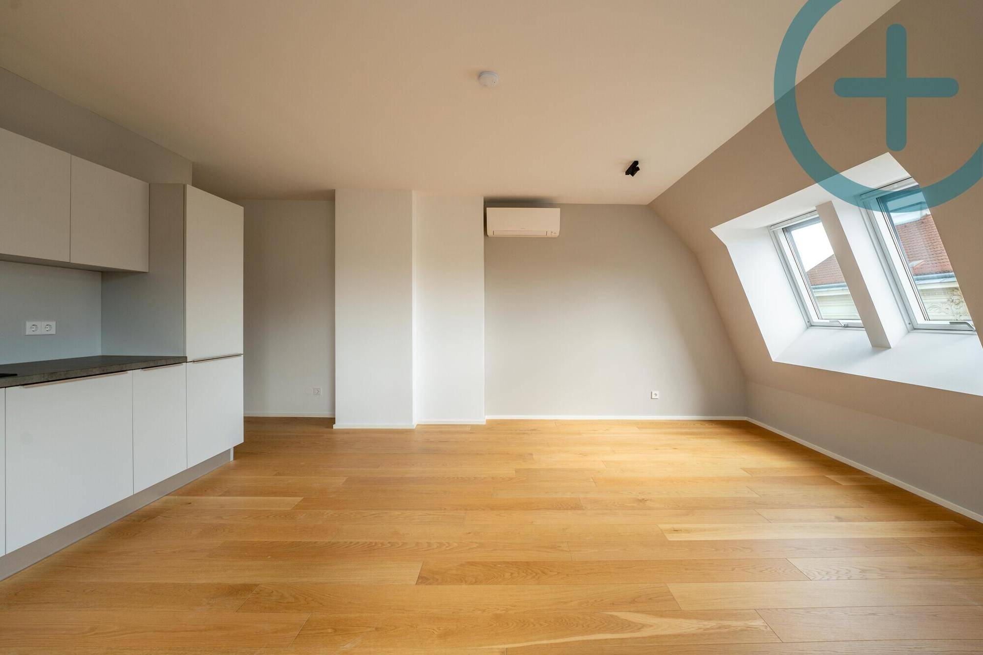 Geräumiger Wohn- und Essbereich mit integrierter Küche, Holzboden und viel Tageslicht durch die Dachfenster.