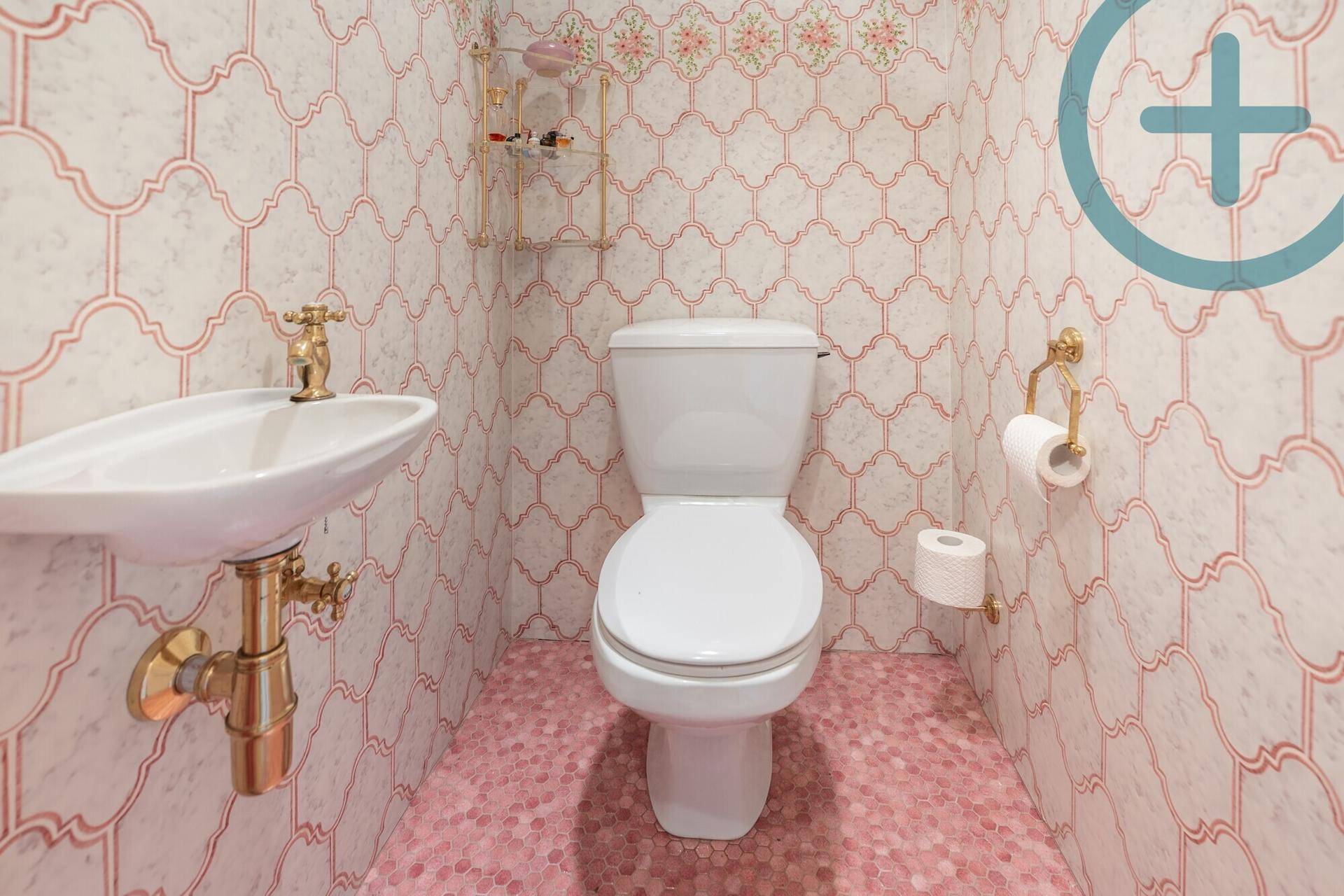 Kleines Gäste-WC mit auffälligen rosa Fliesen und goldenen Armaturen.
