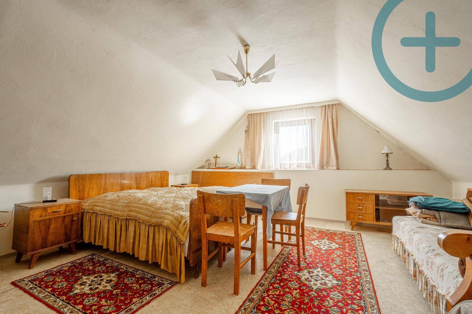 Gemütliches Schlafzimmer im Dachgeschoss mit Doppelbett, Teppichen und schrägen Wänden.