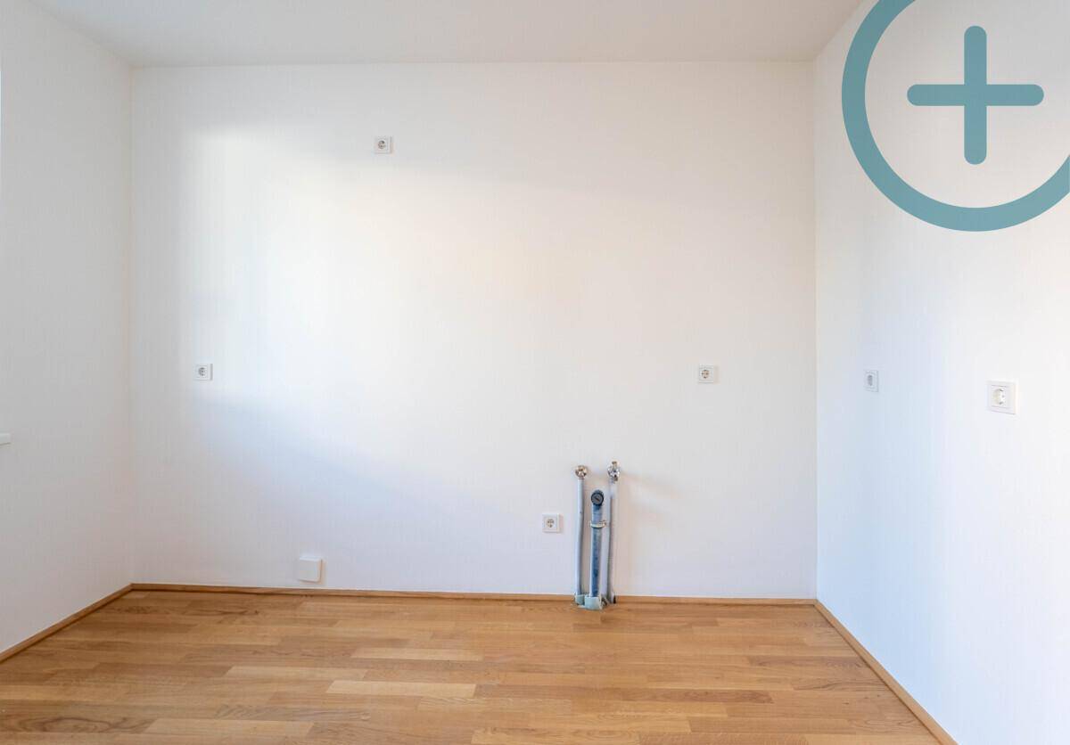 Leerer Raum mit Anschlüssen für eine Küche und hellem Parkettboden, bereit zur Installation.