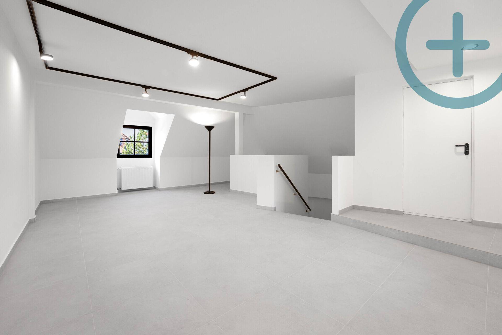 Geräumiger, leerer Raum mit Fliesenboden, Dachschrägen und einer modernen Stehlampe.
