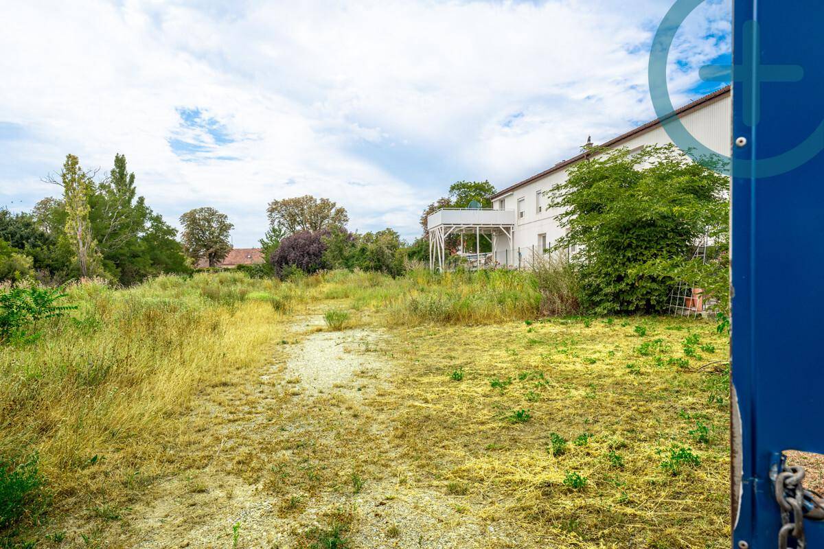Weitläufiges, unbebautes Grundstück mit hohem Gras und einem Gebäude mit Balkon im Hintergrund.