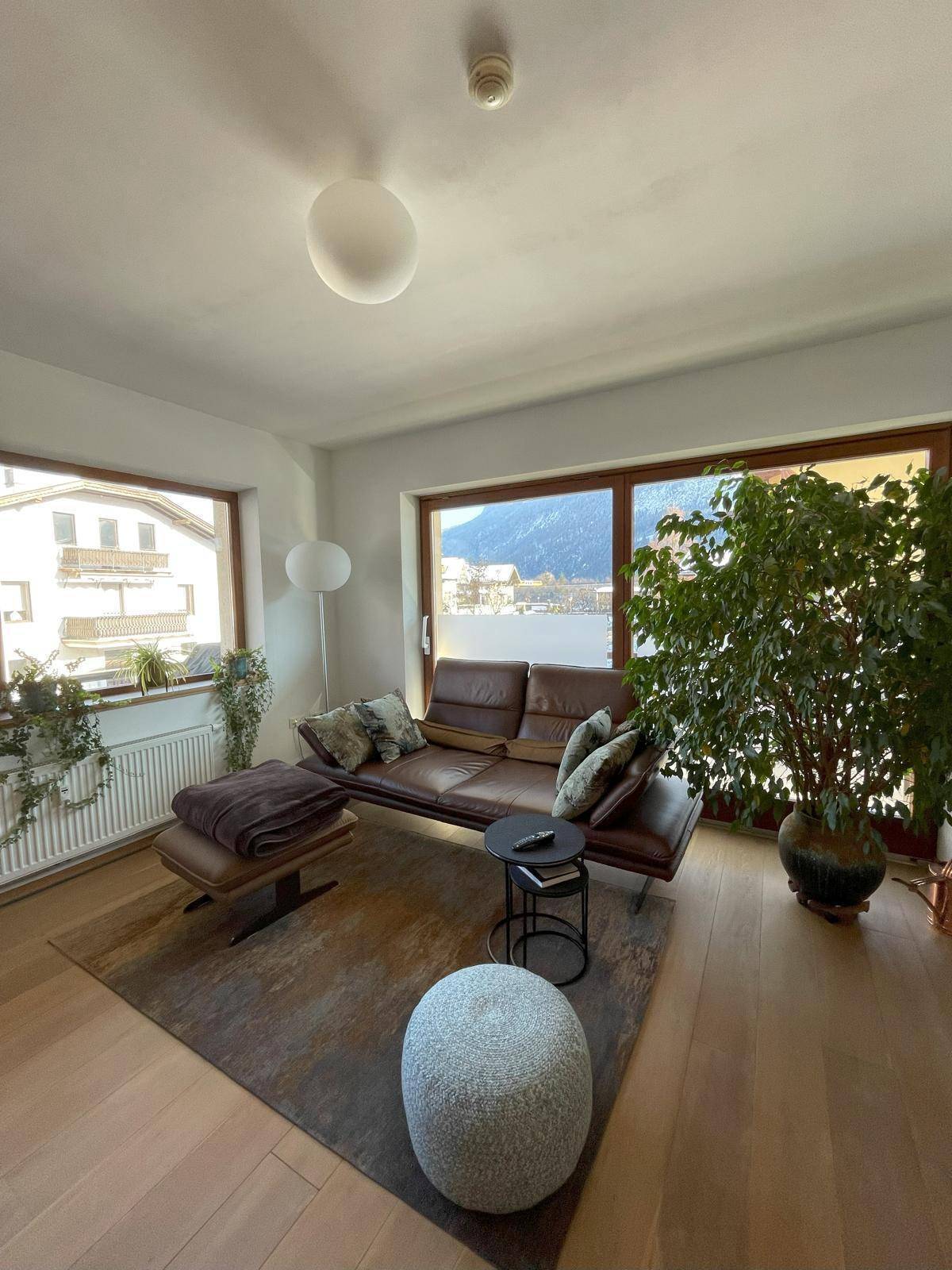 Gemütliches Wohnzimmer mit Ledersofa, Holzboden und großen Fenstern mit Bergblick.