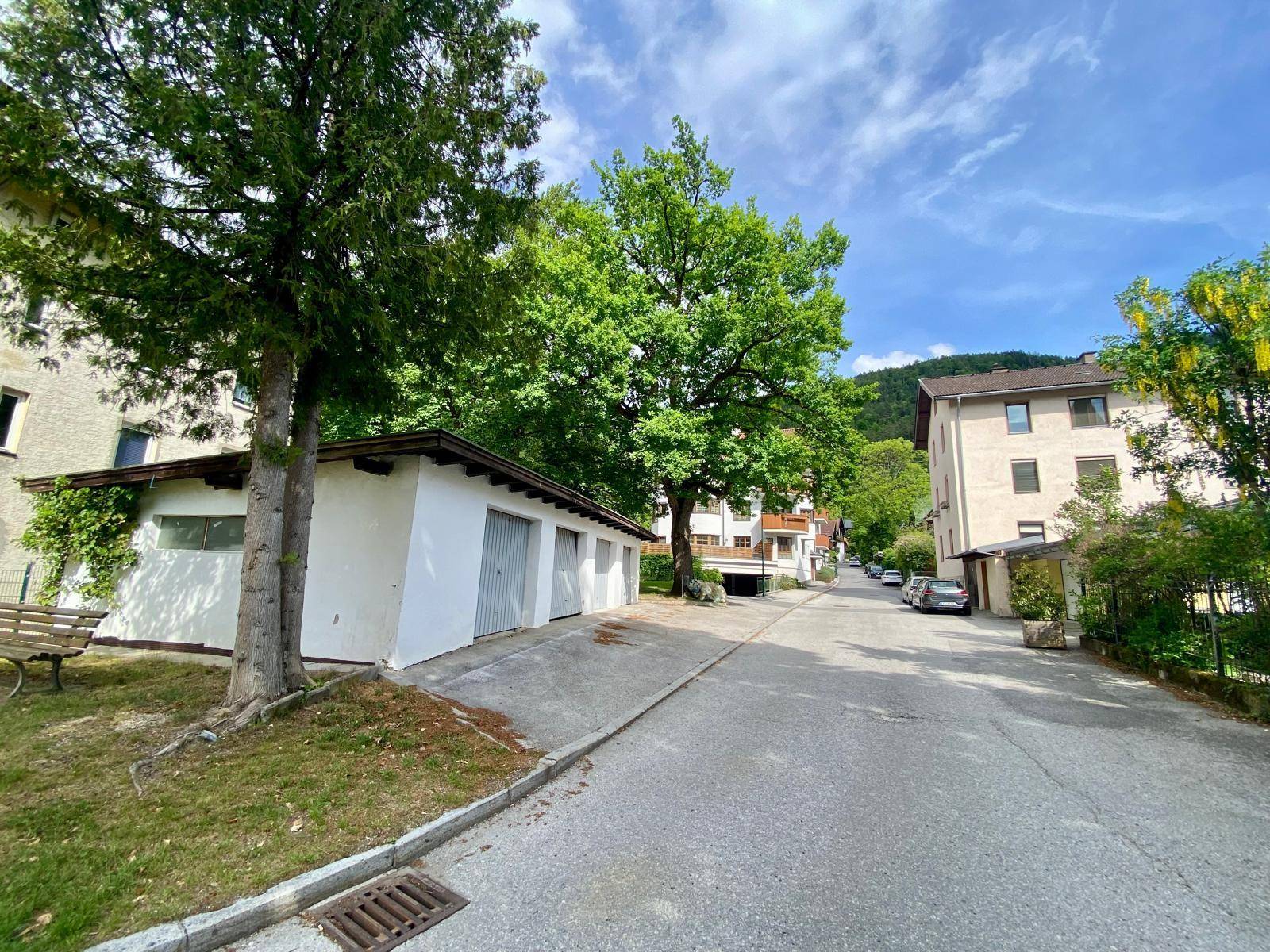 Wohnstraße mit Garagengebäude und weiteren Häusern, umgeben von viel Grün und Bäumen.