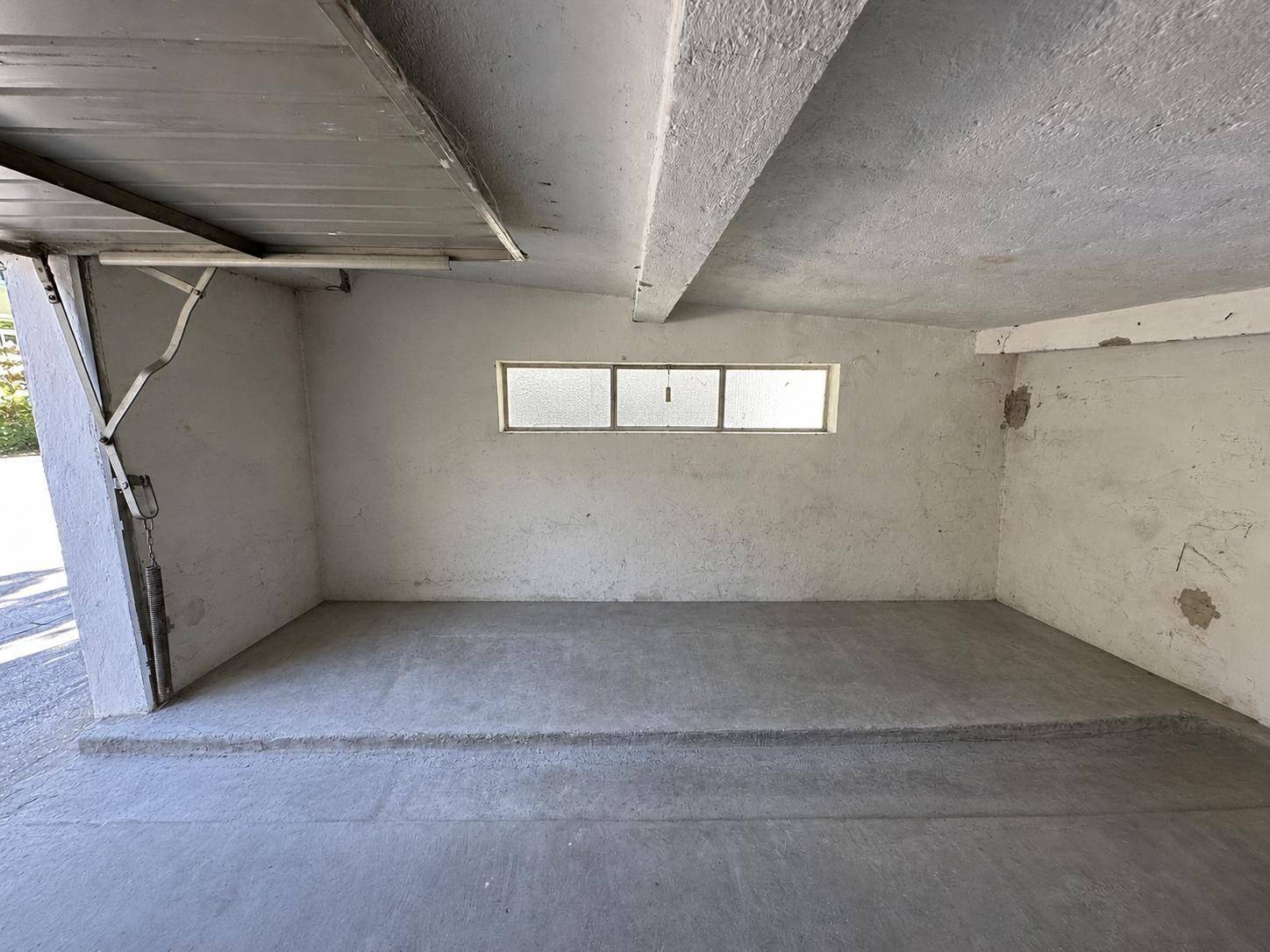 Geräumige, leere Garagenbox mit Betonboden und einem schmalen Fensterband für natürliches Licht.