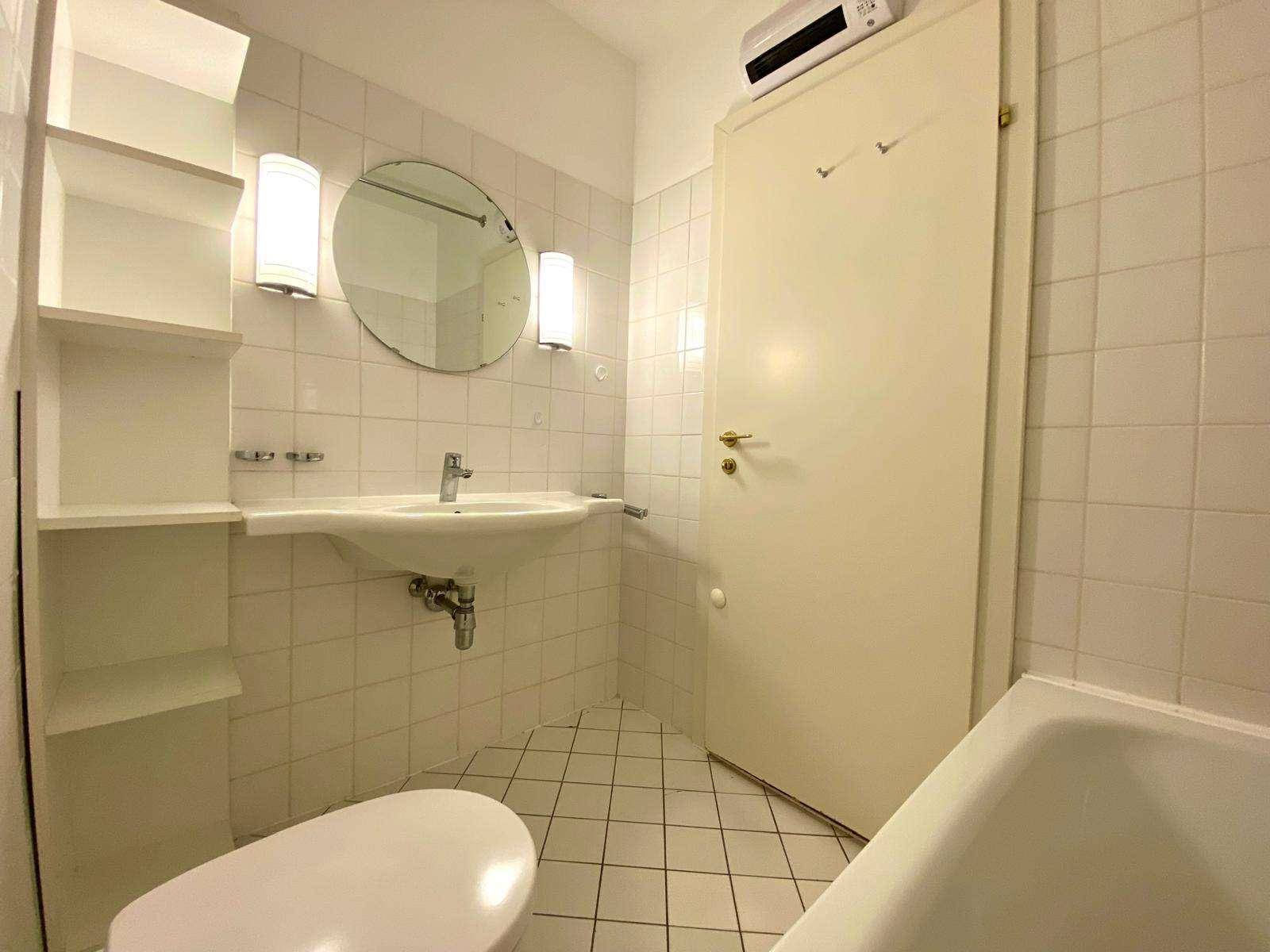 Badezimmer mit weißen Fliesen, Waschbecken, Toilette und einer Badewanne.