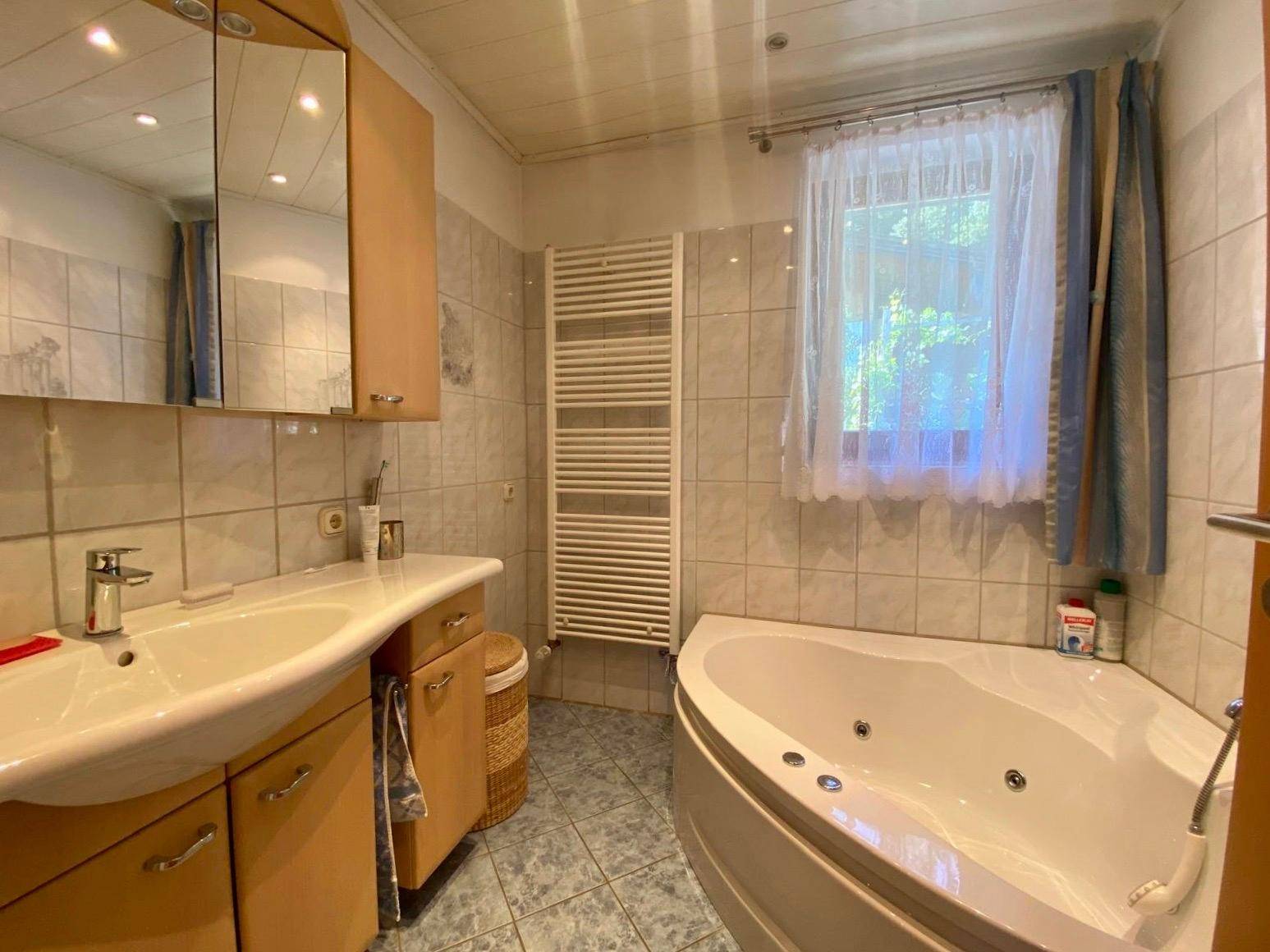 Gefliestes Badezimmer mit Eckbadewanne, Einzelwaschbecken und beheiztem Handtuchhalter.
