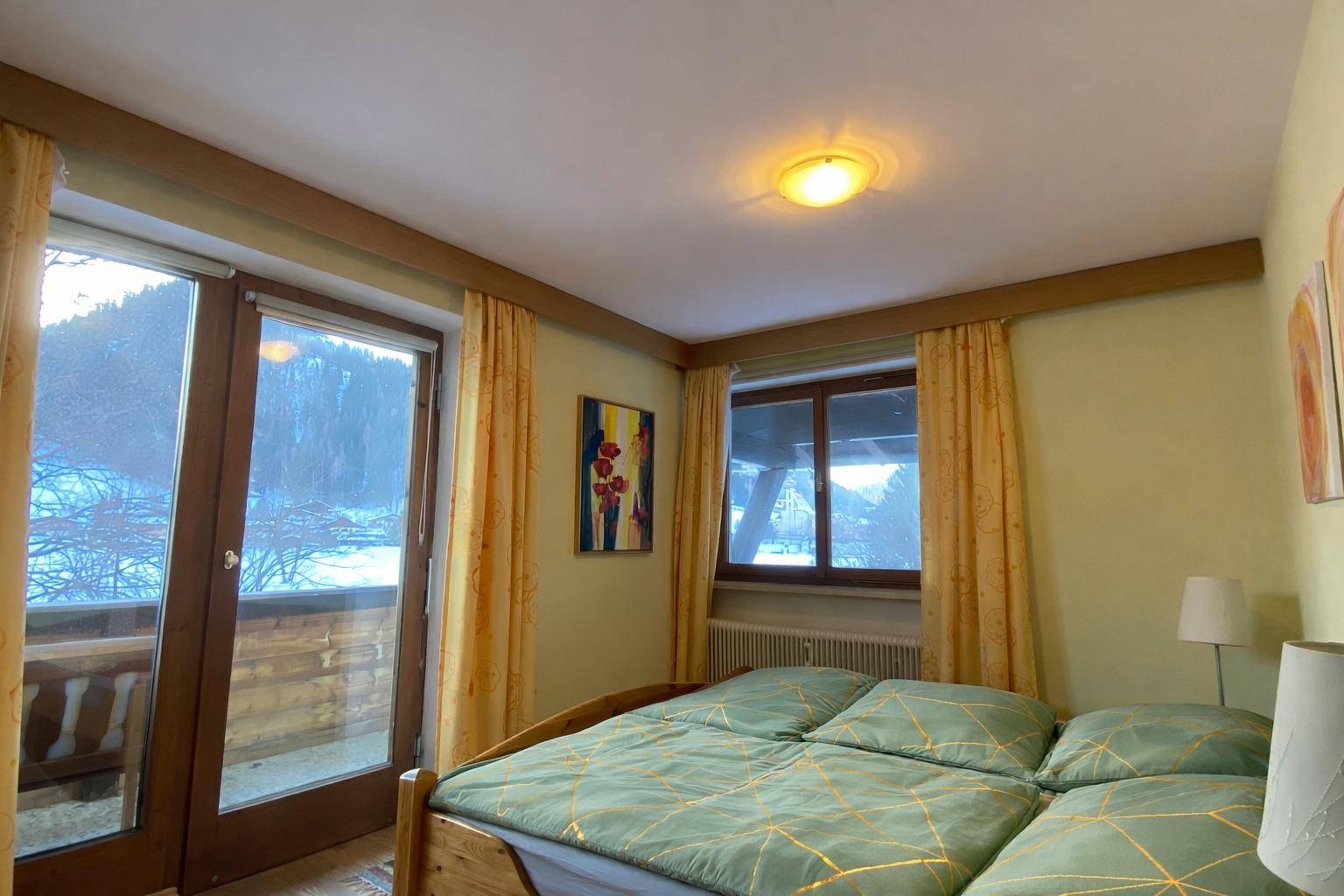 Schlafzimmer mit Doppelbett, Balkonzugang und Blick auf die verschneite Landschaft.