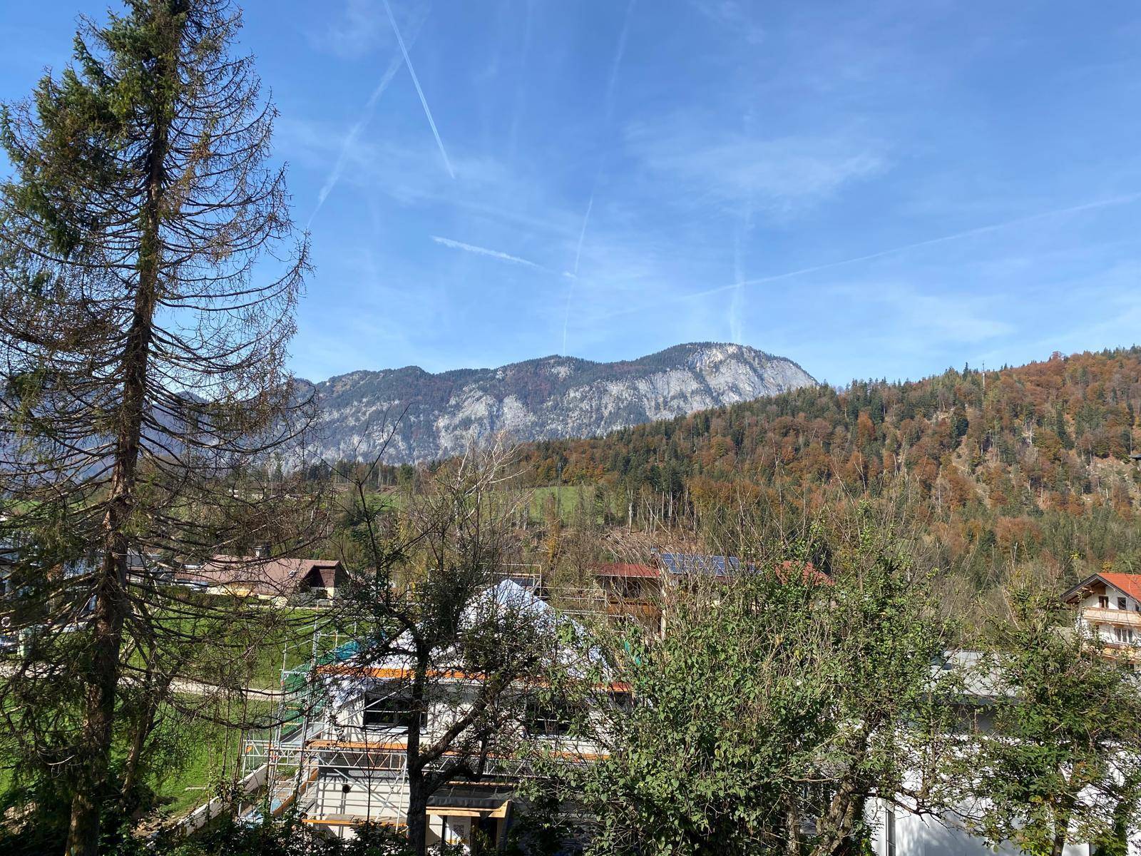 Weitläufiger Blick auf die umliegende Berglandschaft und herbstliche Wälder unter blauem Himmel.
